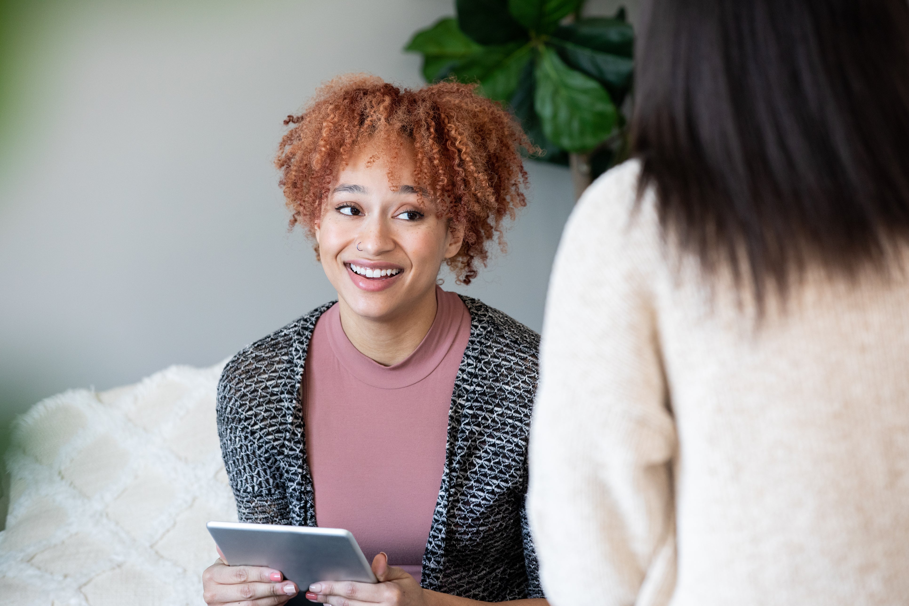 Woman holding a tablet and smiling at another person in an indoor setting
